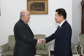 Deux hommes en costume se serrent la main dans un cadre officiel.