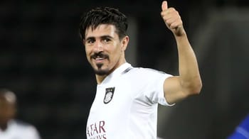 Footballer Baghdad Bounedjah en tenue blanche, saluant la foule.