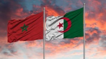 Drapeaux du Maroc et d'Algérie flottant au vent contre un ciel de coucher de soleil.