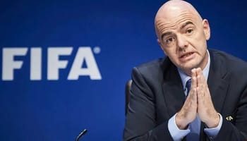 Président de la FIFA en conférence, gestuelle sérieuse.