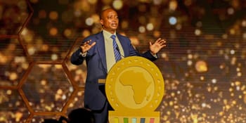 Homme en costume lors d'une conférence sur la CAN 2025 au Maroc.