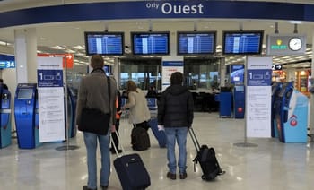 Voyageurs à l'aéroport d'Orly avec valises et écrans d'information.