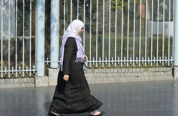 Femme en hijab marchant près d'une clôture en métal en France.