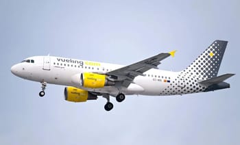 Avion Vueling blanc avec logo jaune en vol dans le ciel gris.