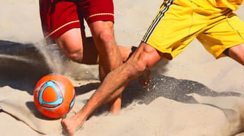 Joueurs de beach soccer en action sur la plage avec un ballon orange.