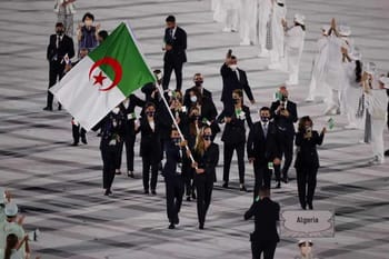 Groupe d'athlètes algériens en tenue de cérémonie avec drapeau national.