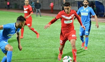 Joueur en rouge contrôlant le ballon lors d'un match de football.
