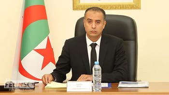 Walid Sadi assis à une table avec drapeau algérien en arrière-plan.