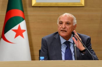 Ahmed Attaf parlant lors d'une conférence avec drapeau algérien en arrière-plan.