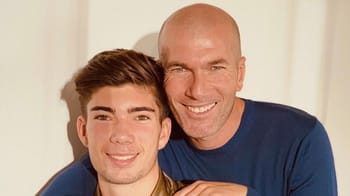 Zidane souriant avec un jeune homme dans une pièce lumineuse.