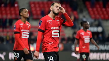 Amine Gouiri en tenue de football rouge, pensif sur le terrain de Rennes.