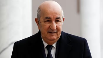 Homme politique algérien en réunion, visage sérieux, costume noir.