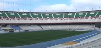 Stade 5 Juillet avec pelouse endommagée et tribunes vides.