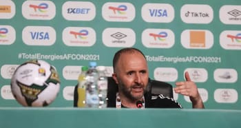 Djamel Belmadi lors d'une conférence de presse avec le logo de la CAN 2021 en arrière-plan.