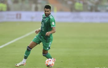 Riyad Mahrez en tenue verte sur le terrain avec un ballon de football.
