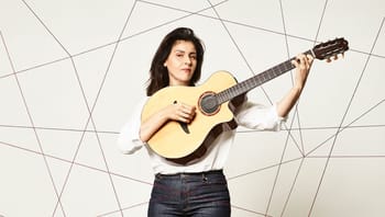 Femme avec guitare acoustique, expression concentrée.