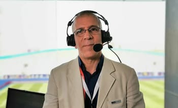 Hafid Derradji avec casque de commentateur dans un stade.