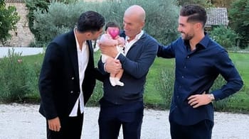 Trois hommes souriants avec un bébé dans un jardin paisible.