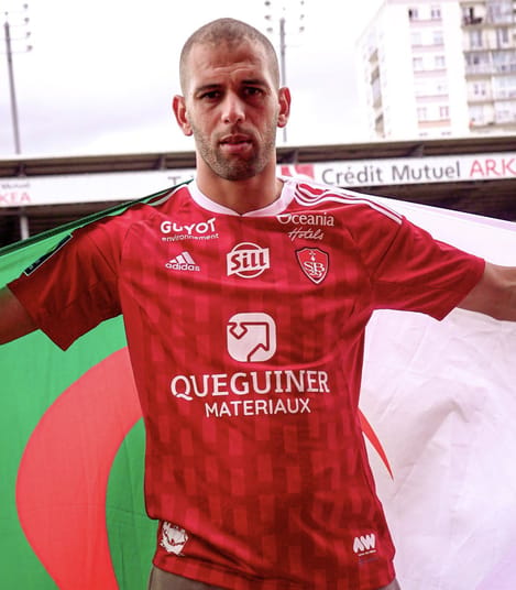 Brest - Montpellier : Slimani convoqué ! Footballeur en maillot rouge avec logos et sponsors.