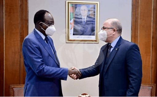 Benabderrahmane reçoit le ministre nigérien de l'intérieur et de la décentralisation Deux hommes en costume se serrent la main dans un bureau avec portrait en arrière-plan.