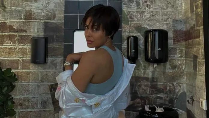 Caroline Chahinez pose dans un lieu public avec mur en briques.