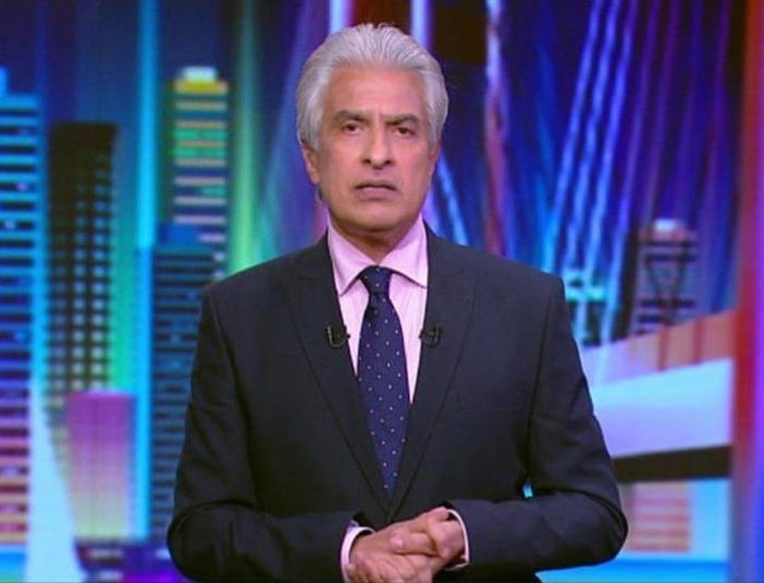 Homme journaliste en costume dans un studio de télévision coloré.