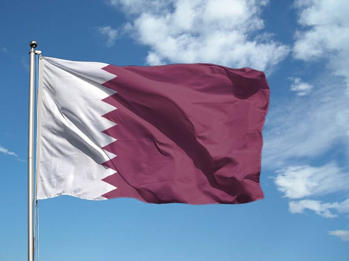 Le Qatar compte investir en Algérie Drapeau du Qatar flottant dans le ciel bleu avec nuages blancs.