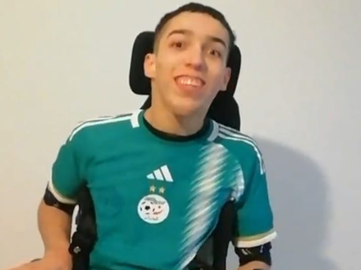 Jeune homme en fauteuil roulant portant un maillot de football algérien.