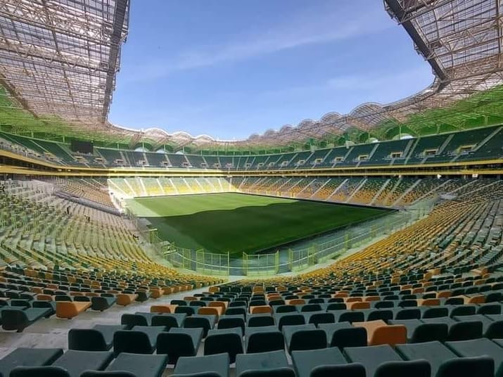 Stade moderne avec sièges colorés et terrain vert au centre.