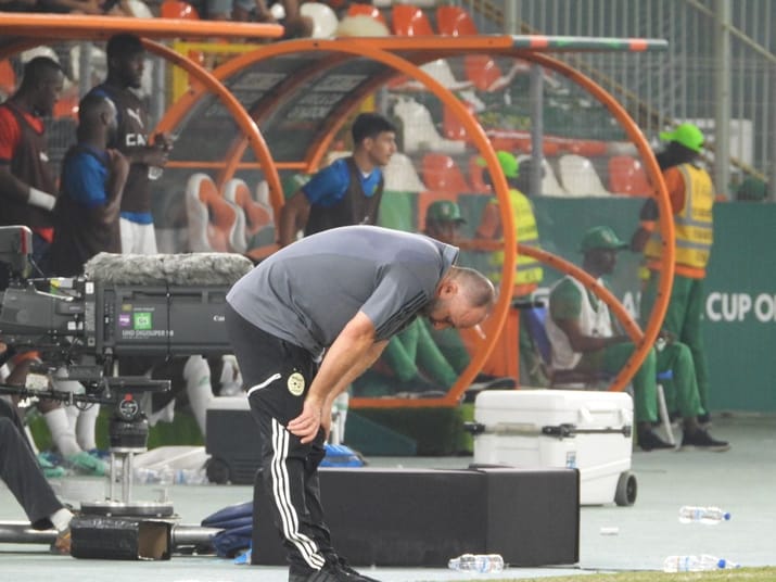 Djamel Belmadi en train de se pencher sur le terrain de football.