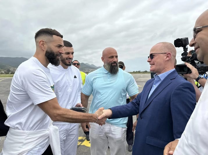 Karim Benzema serre la main d'un homme en costume lors d'une visite en Algérie.