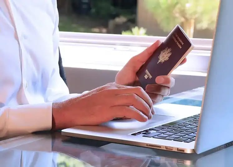 Personne utilisant un ordinateur portable et un passeport pour demander un e-Visa.