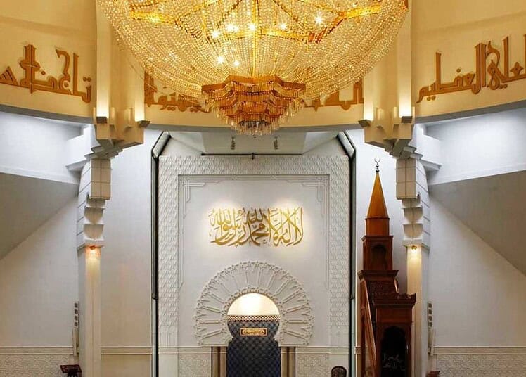 Vue intérieure d'une mosquée avec un chandelier et calligraphies arabes.