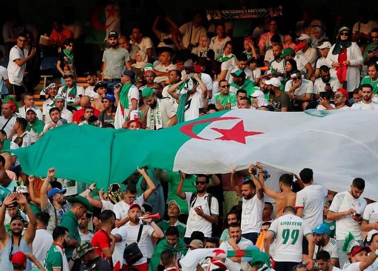 Foule de supporters algériens avec drapeau national lors d'un événement sportif.