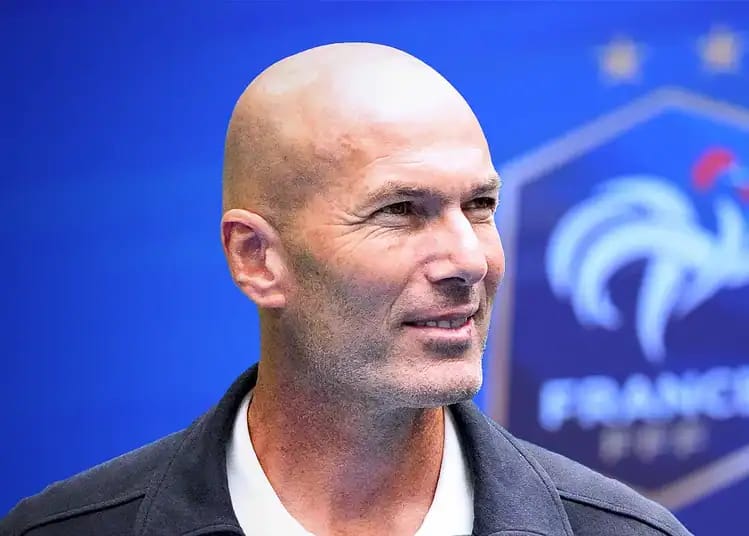 Zinedine Zidane lors d'une conférence, fond bleu avec logo France.