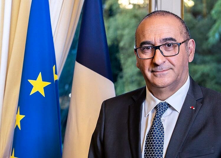 Laurent Nuñez en costume avec drapeaux de l'UE et de la France en arrière-plan.