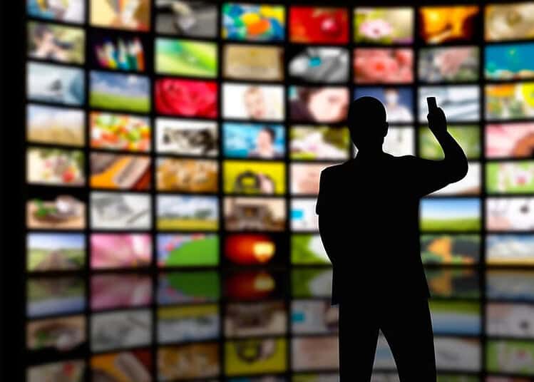 Polémique Ramadan 2026 : Une série algérienne choque Silhouette d'un homme devant un mur d'écrans de télévision.