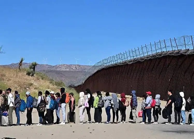 Découvrez le nouveau plan de l'UE sur l'expulsion des sans-papiers Groupe de migrants faisant la queue à la frontière avec une barrière de sécurité.