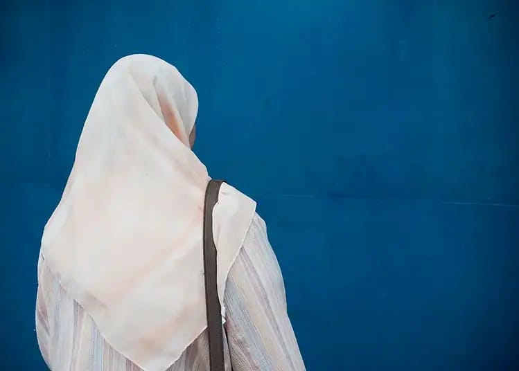 Femme avec hijab blanc vue de dos devant un mur bleu.