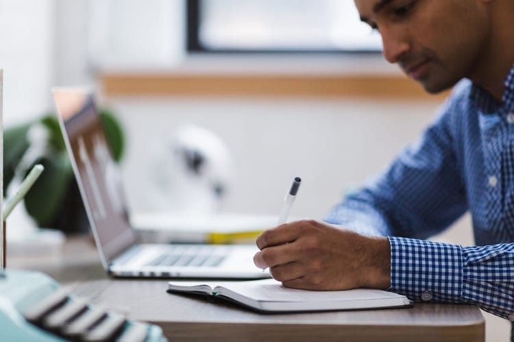 Jeune homme étudiant à son bureau avec ordinateur et cahier.