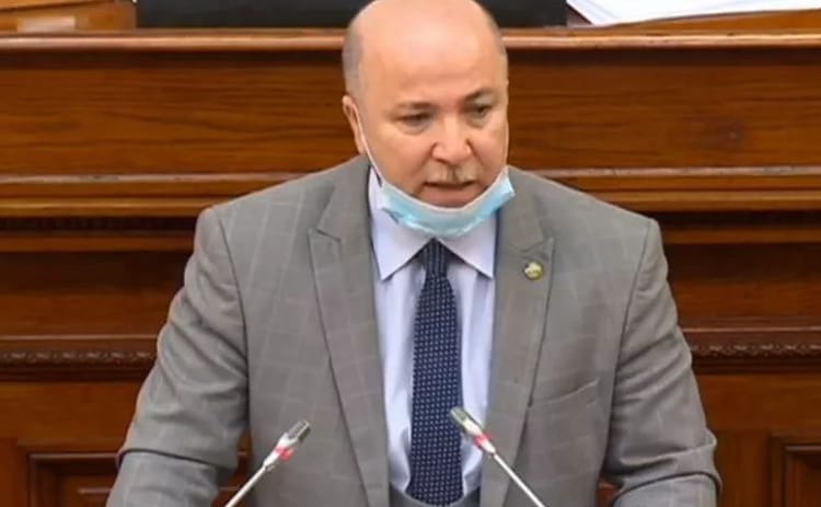 Homme en costume parlant lors d'une réunion gouvernementale.