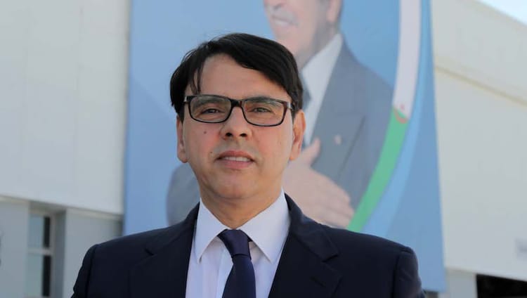 Homme en costume avec lunettes devant un panneau publicitaire.