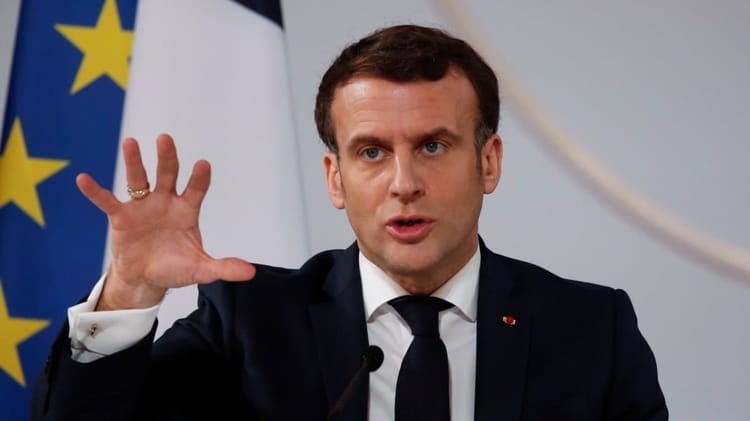 Emmanuel Macron en discours avec drapeaux français et européen en arrière-plan.