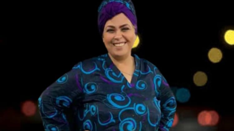 La mise au point de Farida Herhar Femme souriante portant un foulard violet et une robe bleue avec motifs.