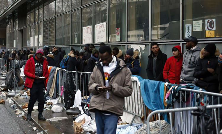 Les sans-papiers victimes de la numérisation des services publics en France Migrants en attente devant un centre d'accueil, vêtements et déchets visibles.