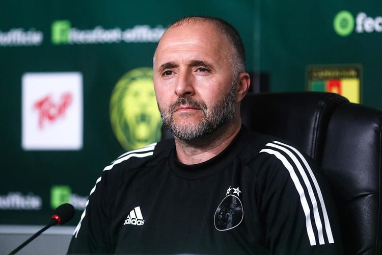 Coach Belmadi en conférence, portant un maillot noir avec logo.