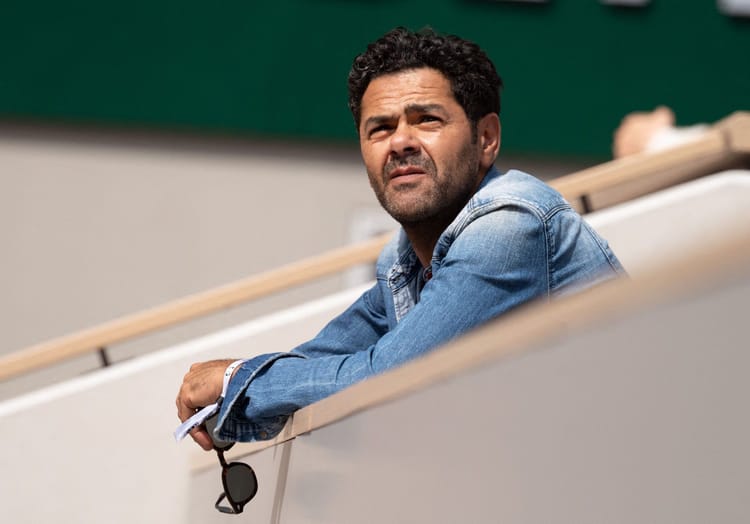 Affaire Gassama : le marocain Jamel Debouze accusé de... Homme méditant dans un stade, regard pensif, ambiance sportive.