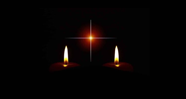 Cierges allumés avec croix lumineuse dans l'obscurité.
