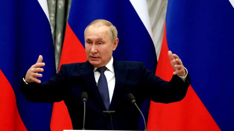 Vladimir Poutine parlant lors d'une conférence avec drapeaux russes en arrière-plan.