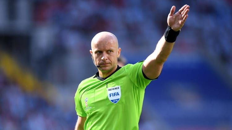 Arbitre FIFA en uniforme vert levant la main sur le terrain.
